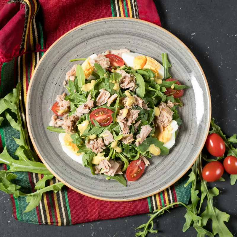 Delicious tuna salad with arugula, cherry tomatoes, and eggs on a decorative plate.