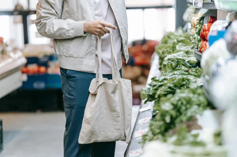 Man selecting fresh vegetables in a grocery store with an eco-friendly bag.