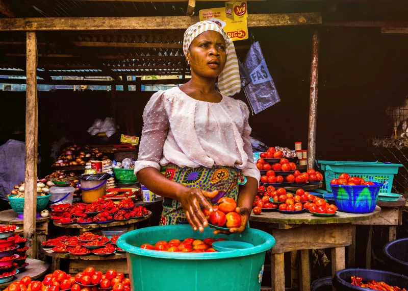 Woman selling fresh tomatoes at an outdoor market stall, showcasing vibrant produce.