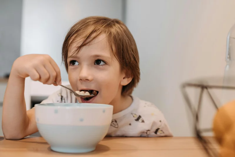 Adorable child enjoying cereal at breakfast indoors with a spoon.