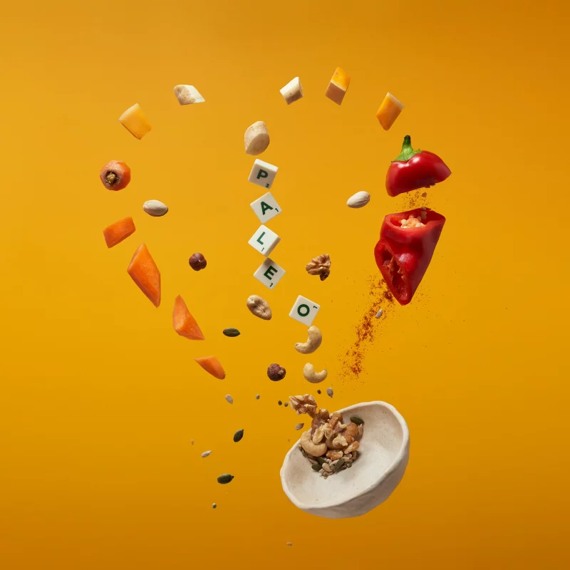 An artistic display of paleo diet foods floating against an orange background