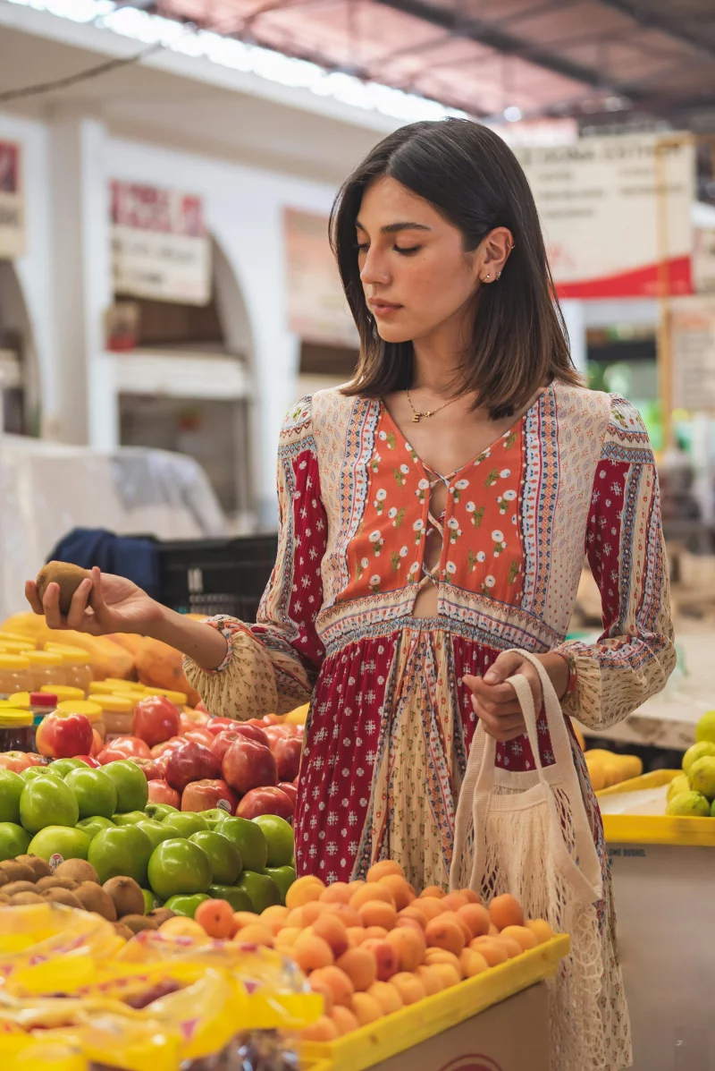 A young woman in a colorful dress selecting fruits at an outdoor market.