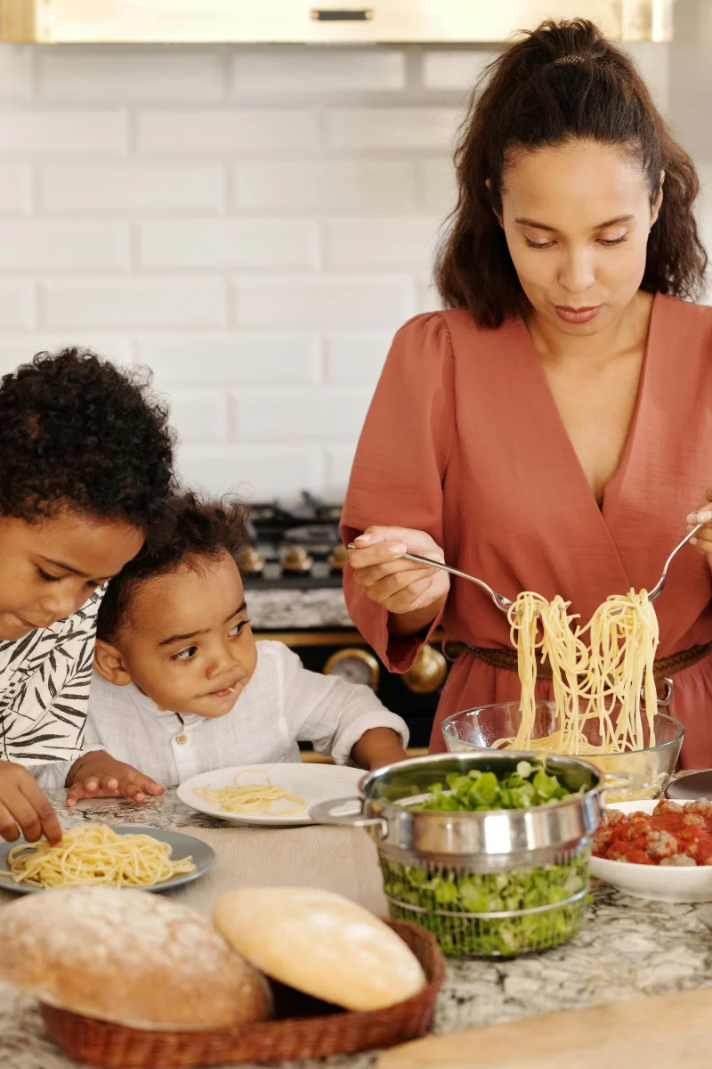 A mother prepares pasta with her children in a modern kitchen, creating a warm family moment indoors.