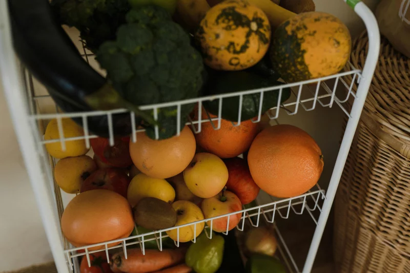 Colorful assortment of fruits and vegetables displayed on a wire shelf in a home setting.