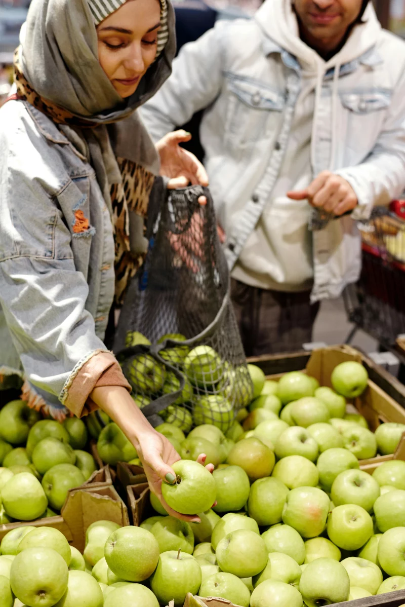 A couple shopping for fresh green apples in an indoor market, showcasing a cultural shopping experience.