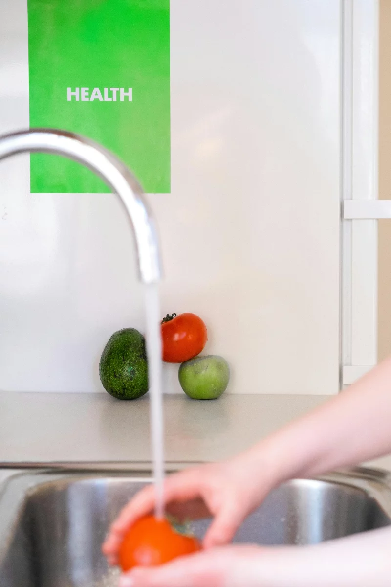 A person washes tomatoes under a faucet, promoting healthy eating and cleanliness.
