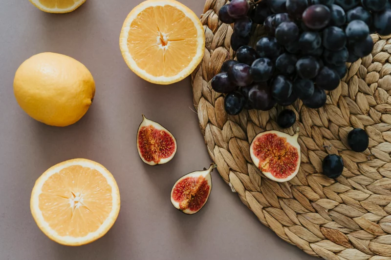A delightful top view of fresh fruits including figs, grapes, and oranges on a woven placemat.
