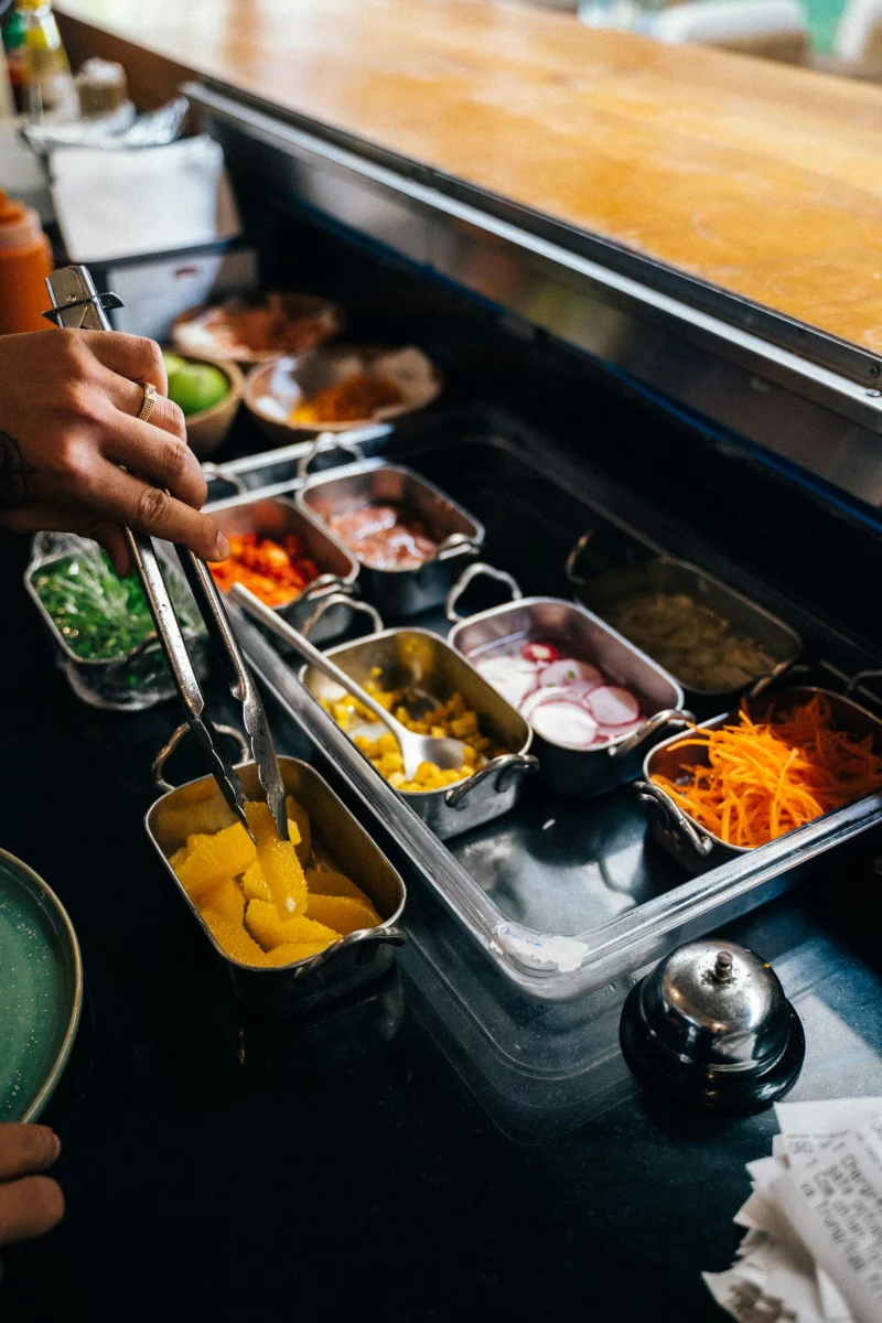 Colorful buffet station with a variety of fresh ingredients in stainless trays.