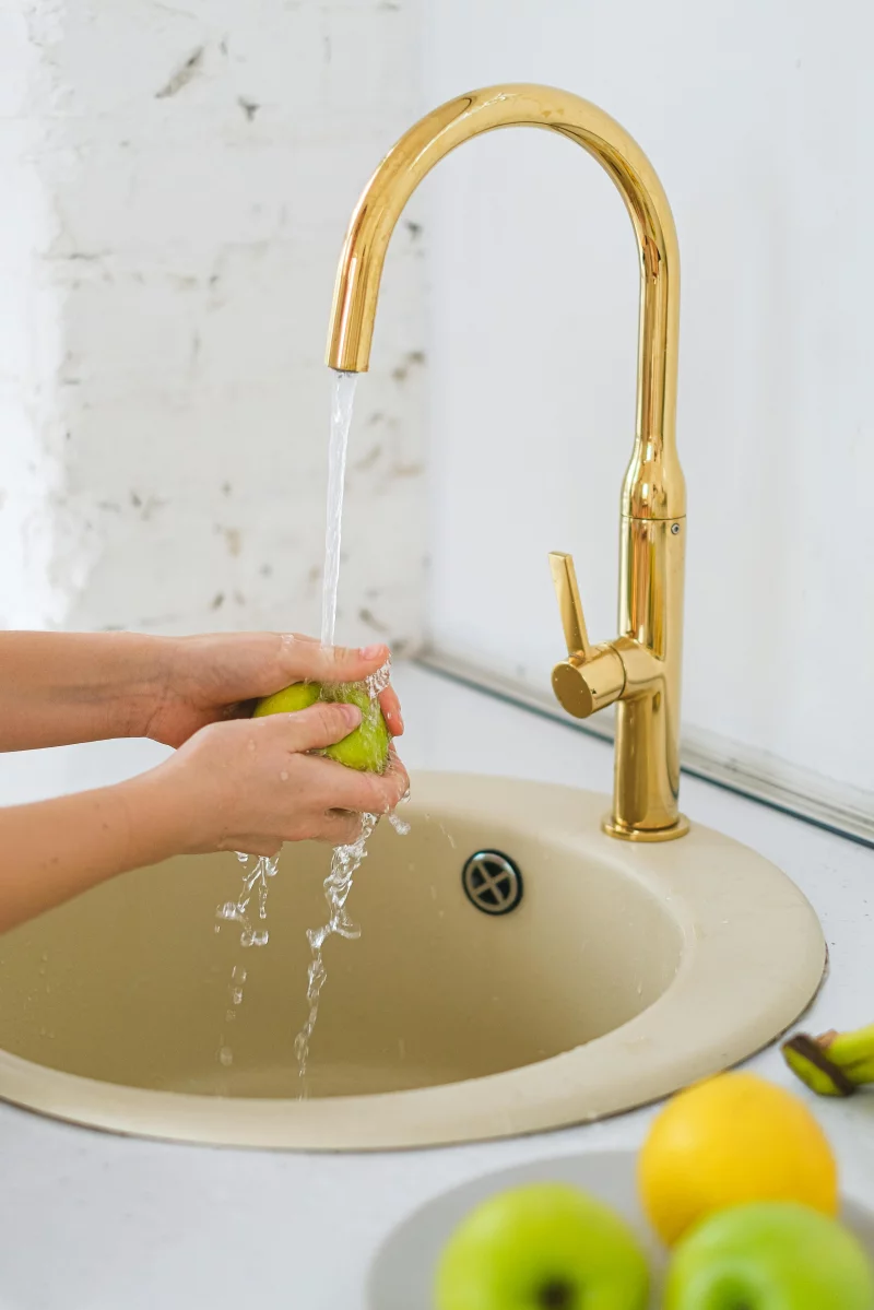 Hands washing a fresh green apple under a gold faucet, promoting healthy eating.