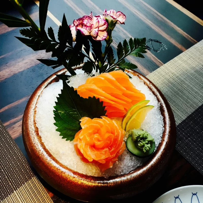 A beautifully presented salmon sashimi dish with flowers and wasabi, perfect for gourmet seafood lovers.