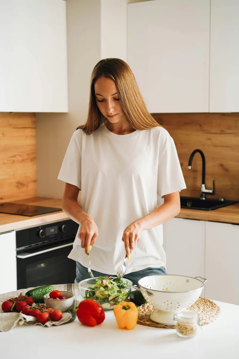A woman preparing a fresh vegetable salad in a modern kitchen for a healthy lifestyle.