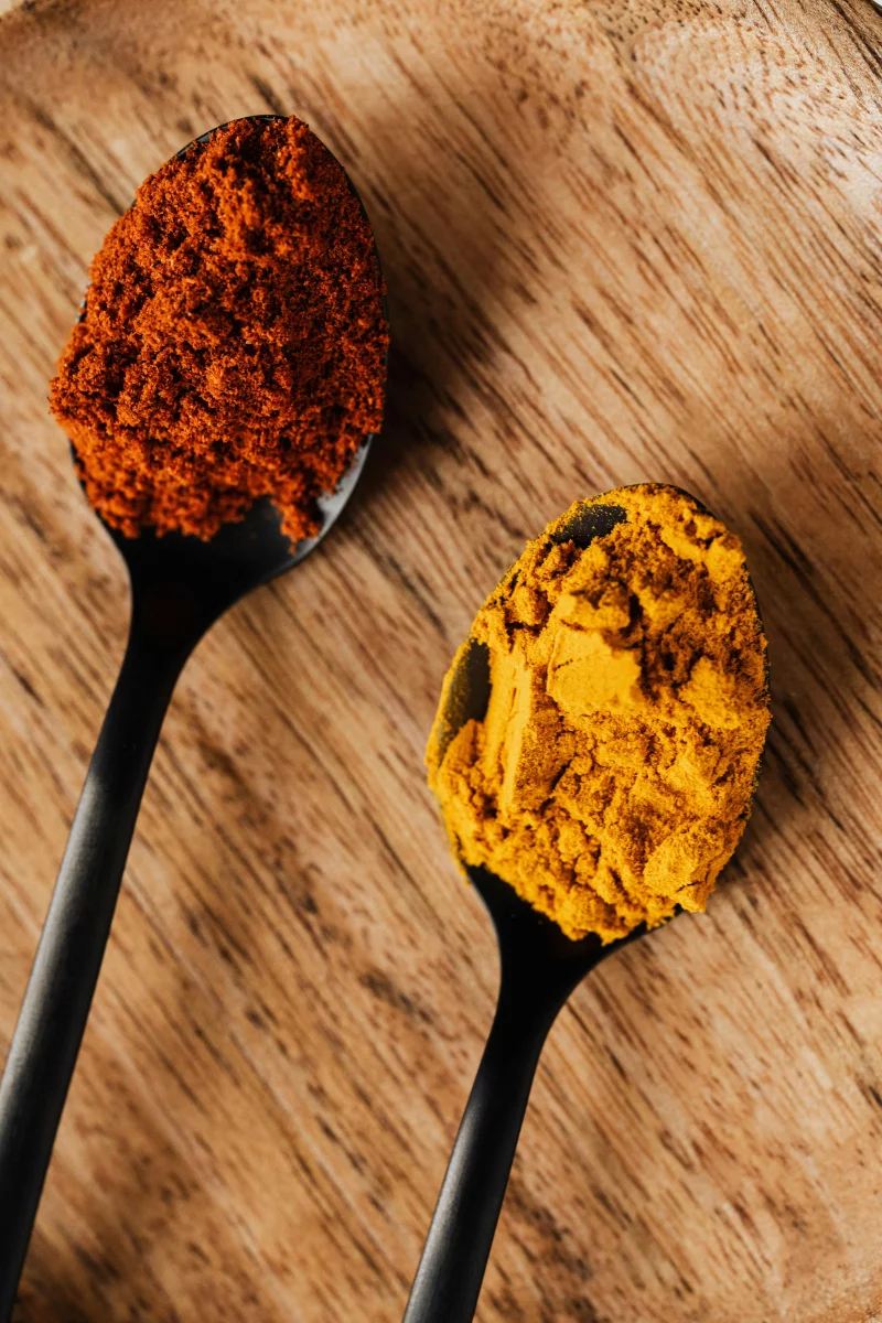 Top view of tablespoons with dry yellow curcuma and hot ground paprika on wooden table