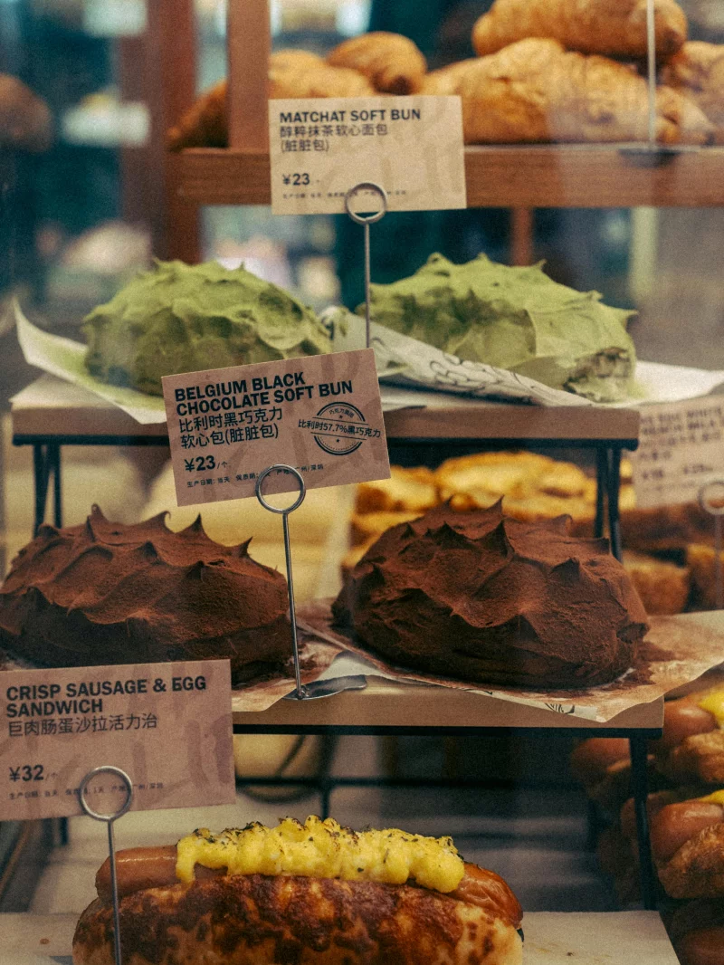 Close-up of assorted bakery buns and sandwiches with visible price tags.