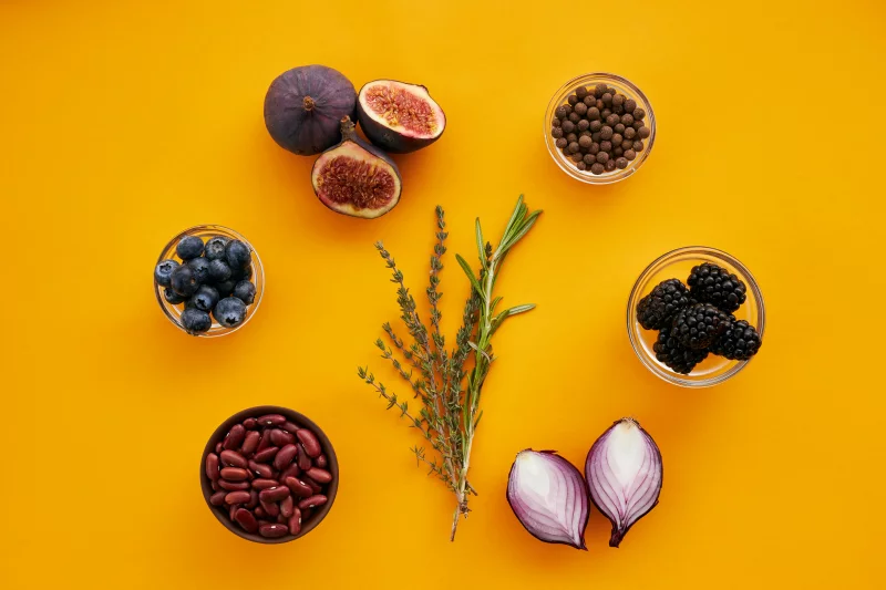 Vibrant flat lay of figs, berries, beans, spices, and herbs on a yellow background.