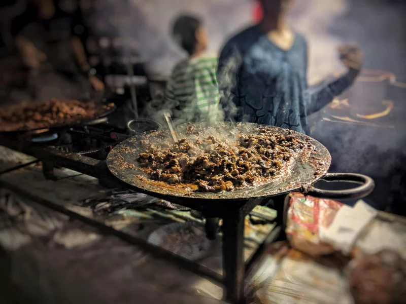A vibrant scene of street food being grilled, showcasing sizzling meat on an open flame.