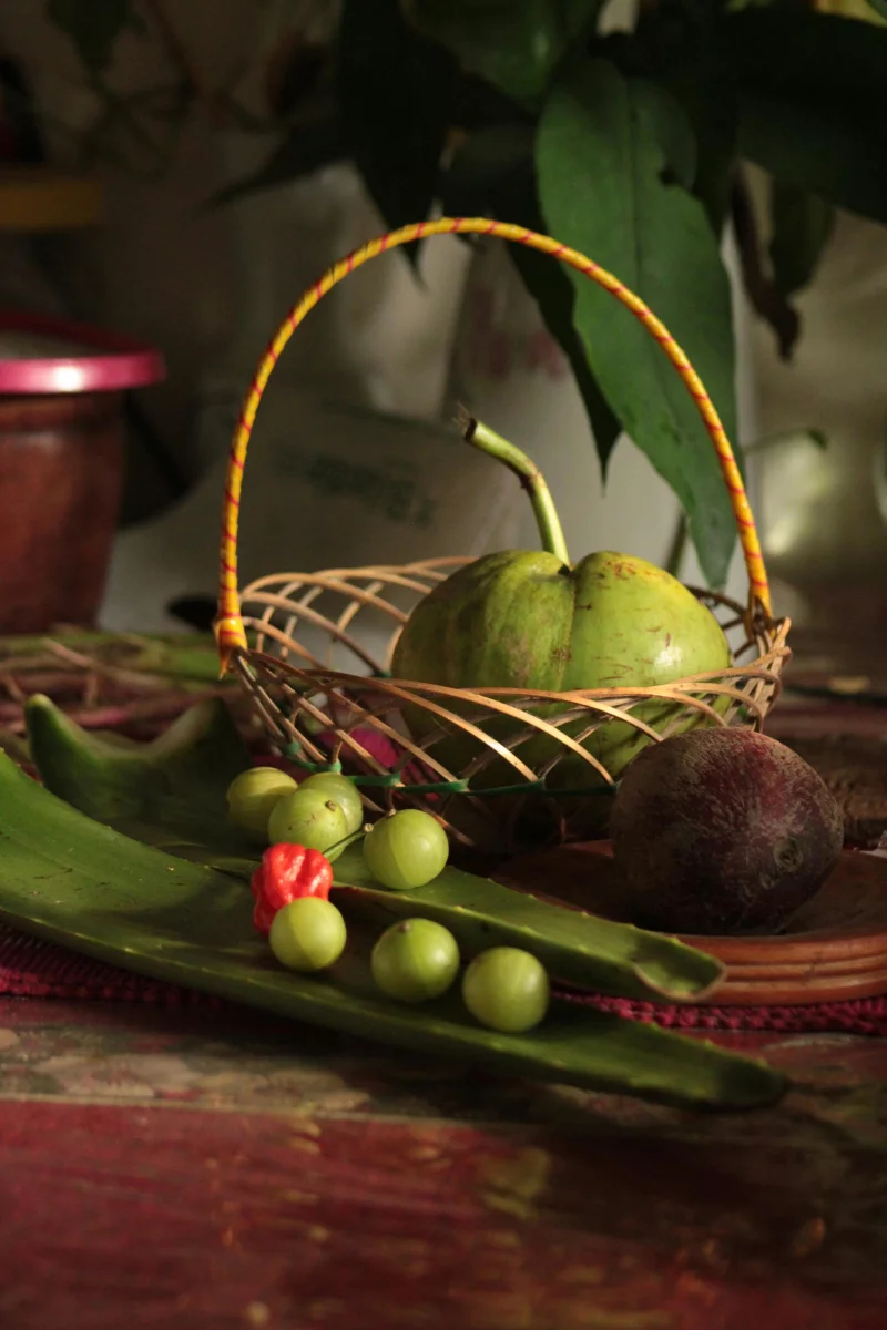 Close-up of a basket with tropical fruits and vegetables on a rustic table.