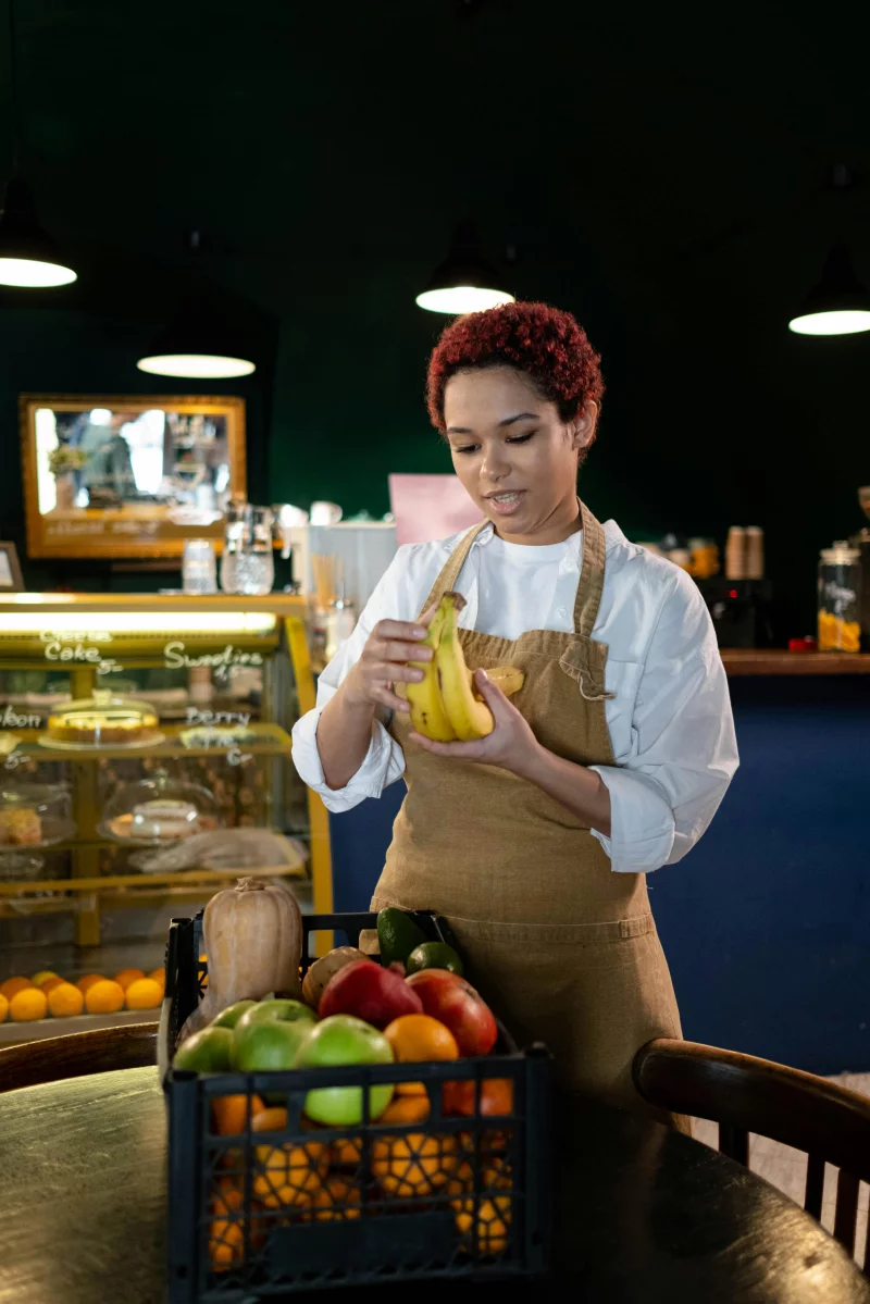 Chef with apron arranging bananas in a cozy café filled with fresh produce.