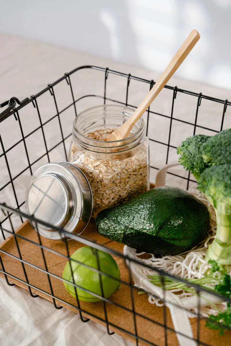 Wire basket with avocado, lime, broccoli, and oatmeal in a glass jar.