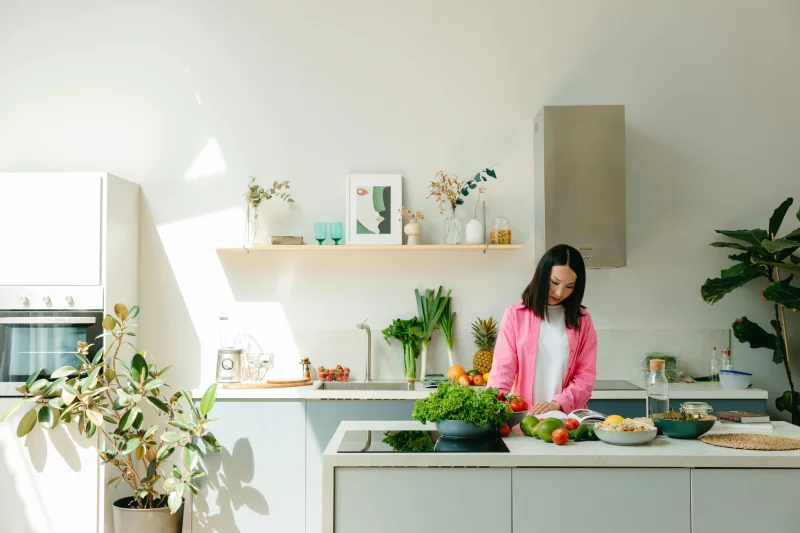 A woman in pink prepares fresh vegetables in a sunlit, modern kitchen, creating a vibrant cooking scene.