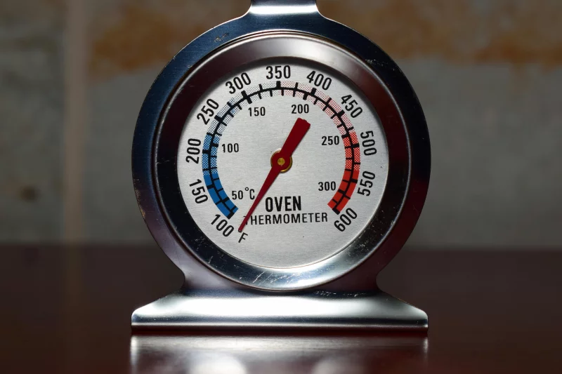 Close-up of a metallic oven thermometer showing temperature in Celsius and Fahrenheit.