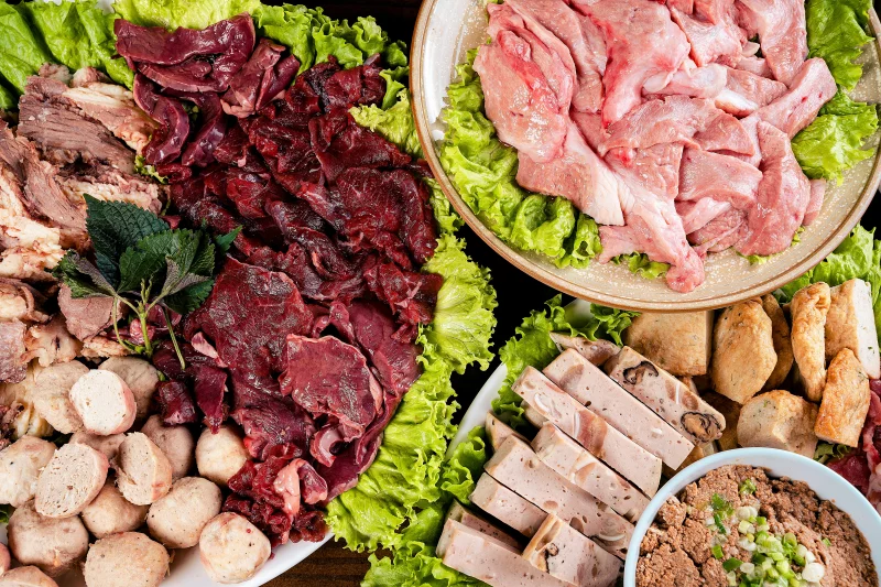 An overhead view of assorted raw meats and ingredients on platters with lettuce.
