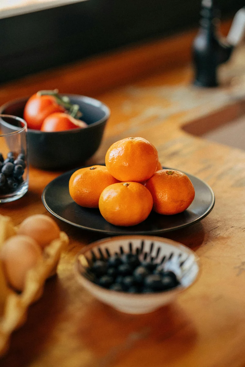 Rustic kitchen setting with fresh oranges, tomatoes, blueberries, and eggs on a wooden counter.