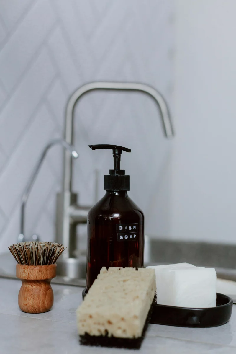 Close-up of kitchen cleaning essentials including dish soap and sponge by a sink.