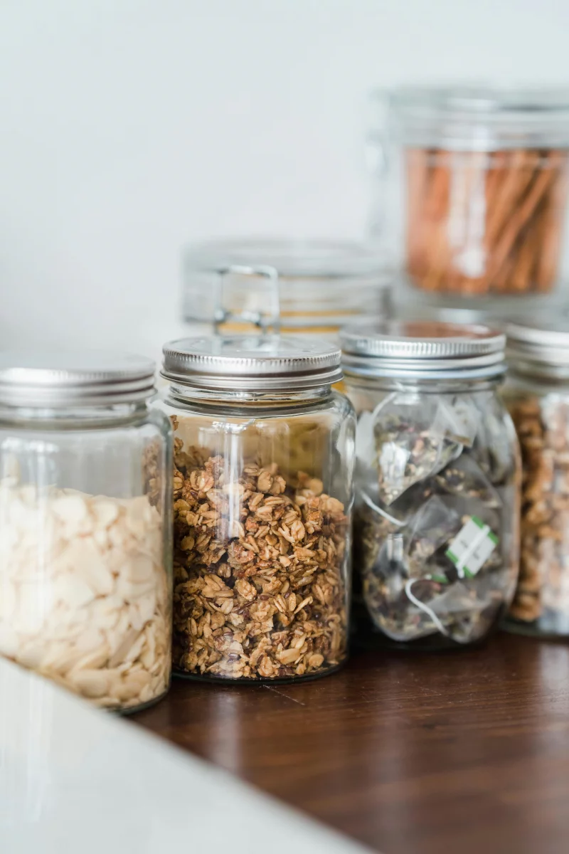 Assorted organic snacks stored in glass jars on a wooden table with a minimalist kitchen theme.