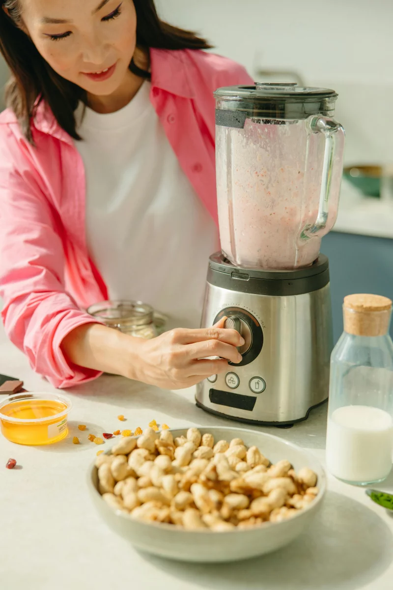 Asian woman in kitchen using blender to make a healthy smoothie with nuts and fruits.