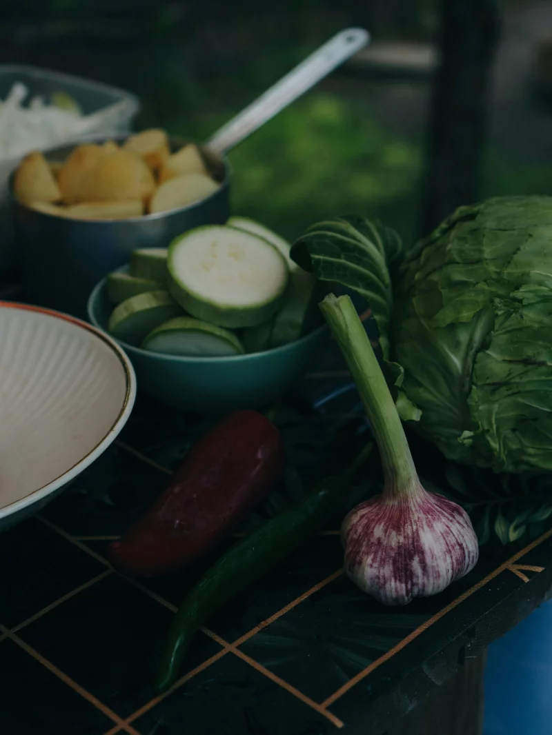 Assortment of fresh vegetables including zucchini, garlic, cabbage, peppers, and potatoes on a kitchen counter.
