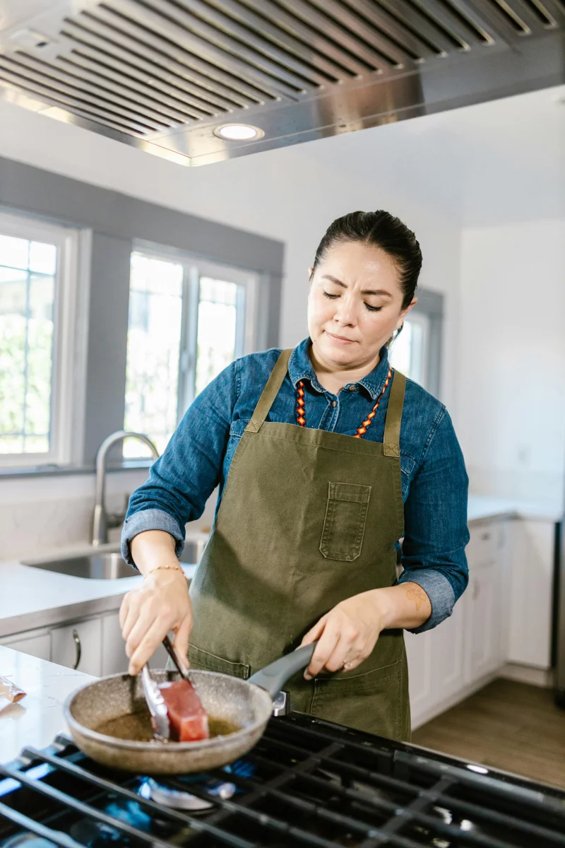 Woman chef frying seafood in modern kitchen setting.