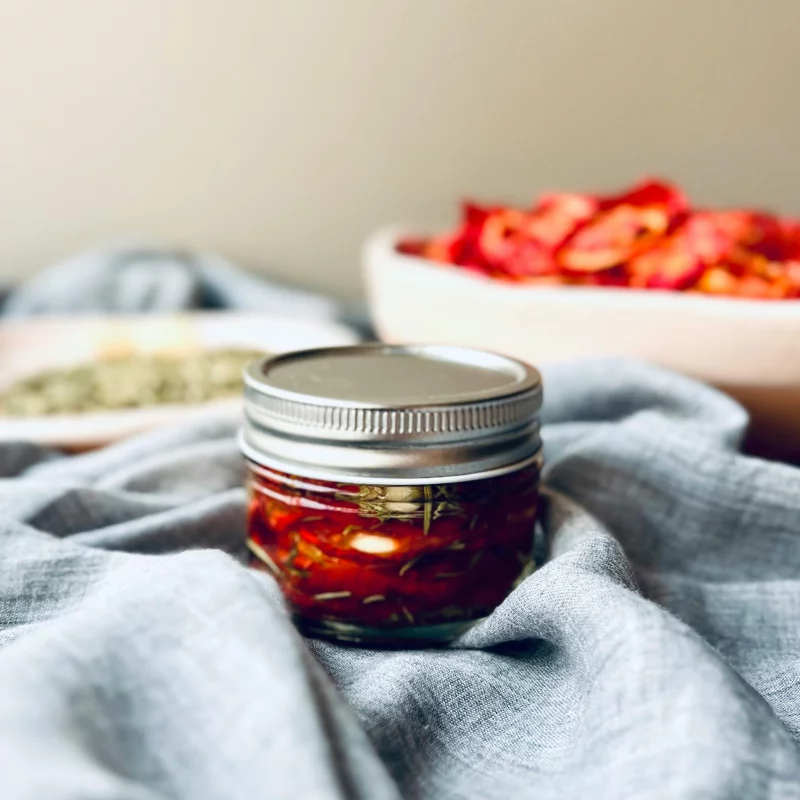 Close-up of a jar with sun-dried tomatoes preserved in oil on cloth background.