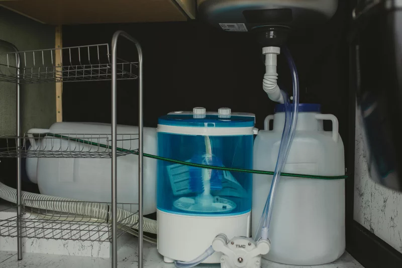 Compact travel-size washer in a storage area with plastic containers and tubing system.