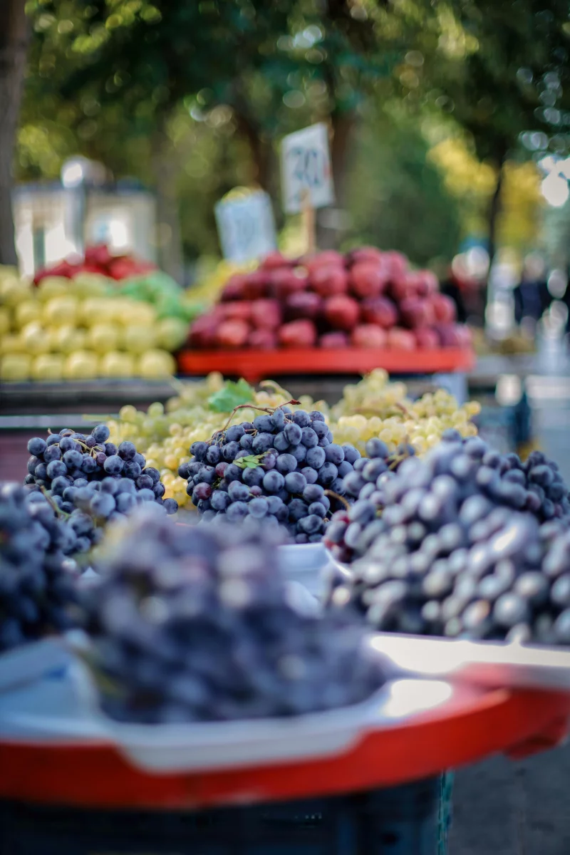 A vibrant display of various fresh fruits at a street market, focusing on grapes in the foreground.