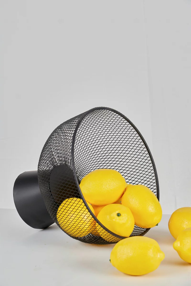 A collection of bright yellow lemons spilling from a stylish metal mesh basket on a white background.