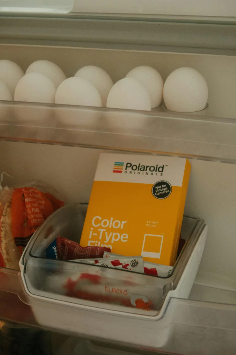 Interior view of a fridge showing a Polaroid film pack and eggs on the shelf.