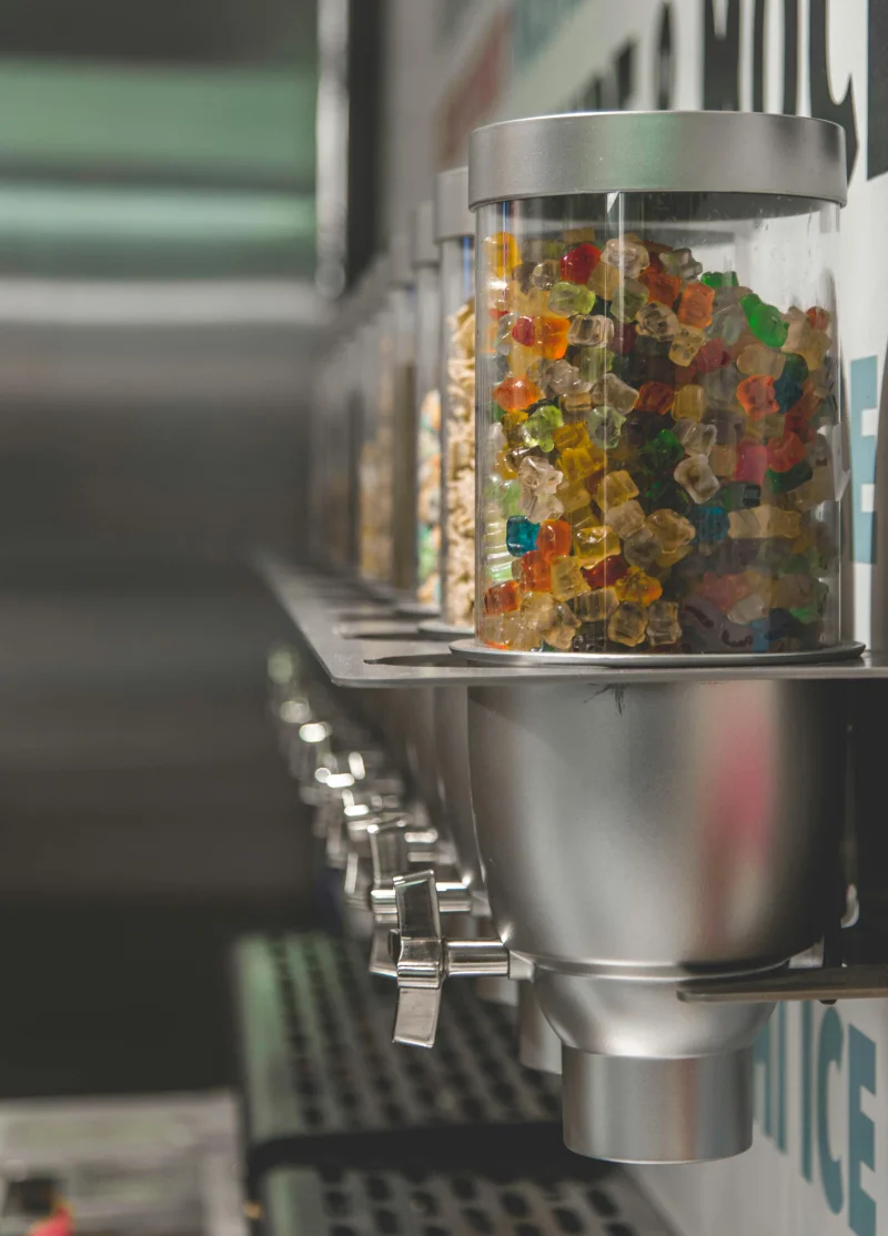 Close-up of colorful gummy bears in modern dispensers within a candy store setting.