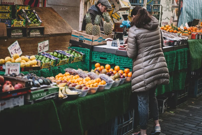 Lively city market stall displaying diverse fresh fruits. A customer browses.