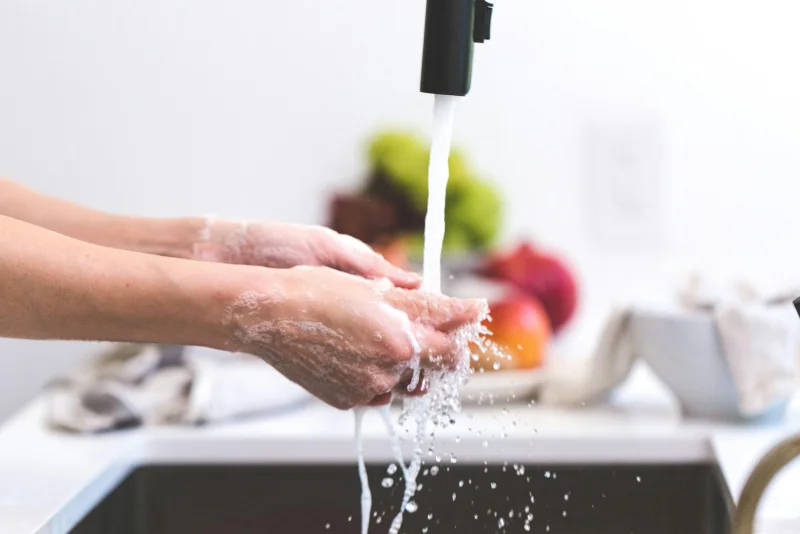 Hands being washed under a tap in a kitchen, promoting hygiene and cleanliness.