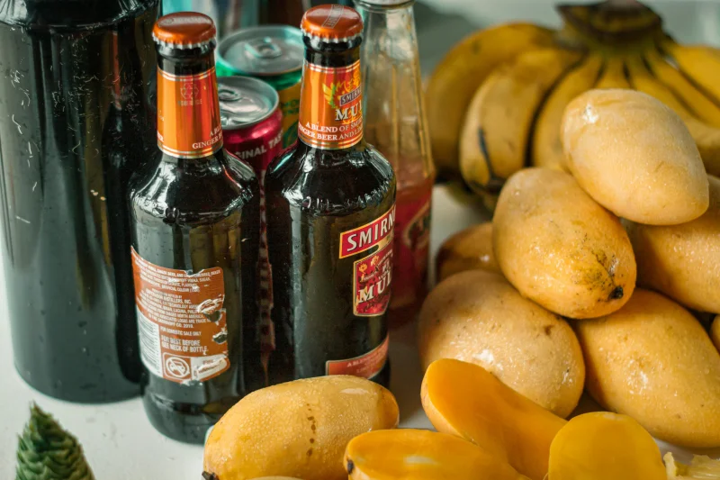 Close-up of assorted beverages and ripe mangoes with banana in background.
