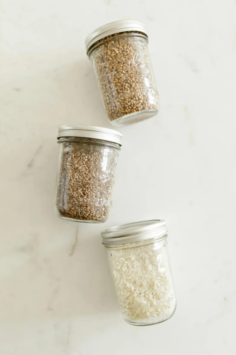Three glass jars with dry goods like grains and rice on a light background.