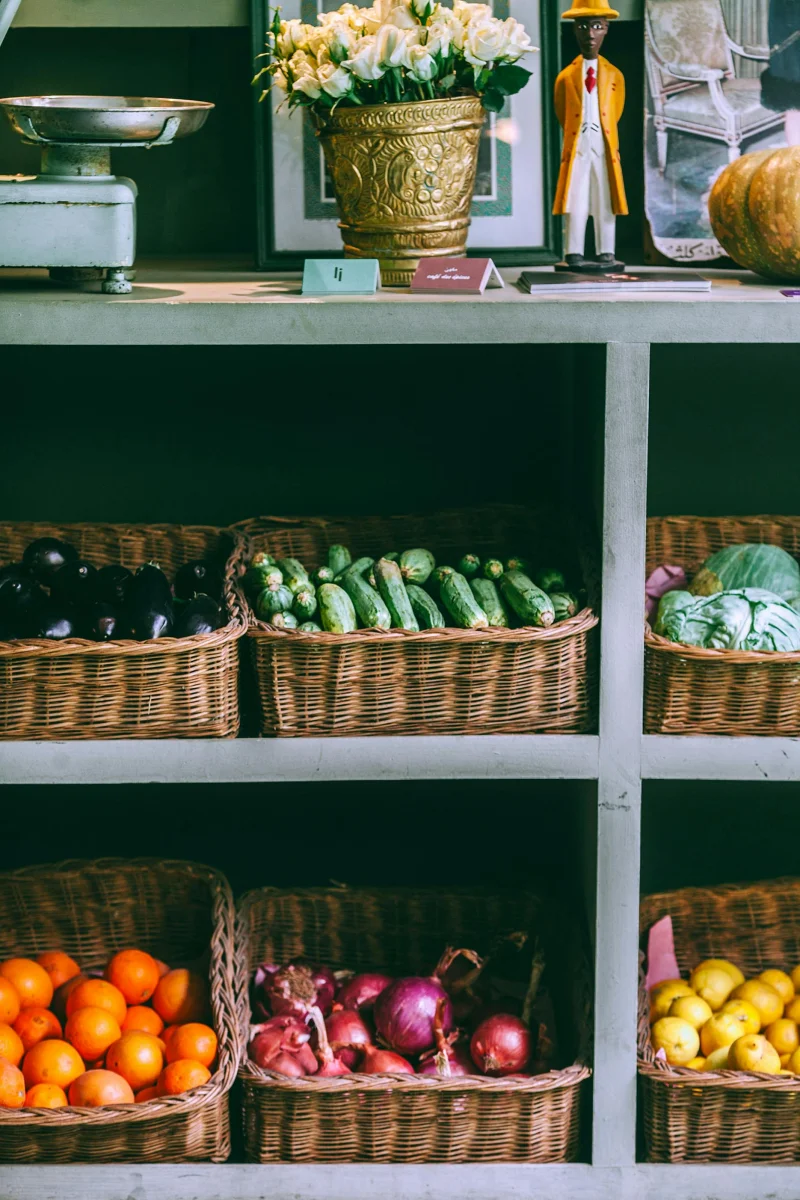 A variety of fresh fruits and vegetables displayed in wicker baskets at an indoor market stall.