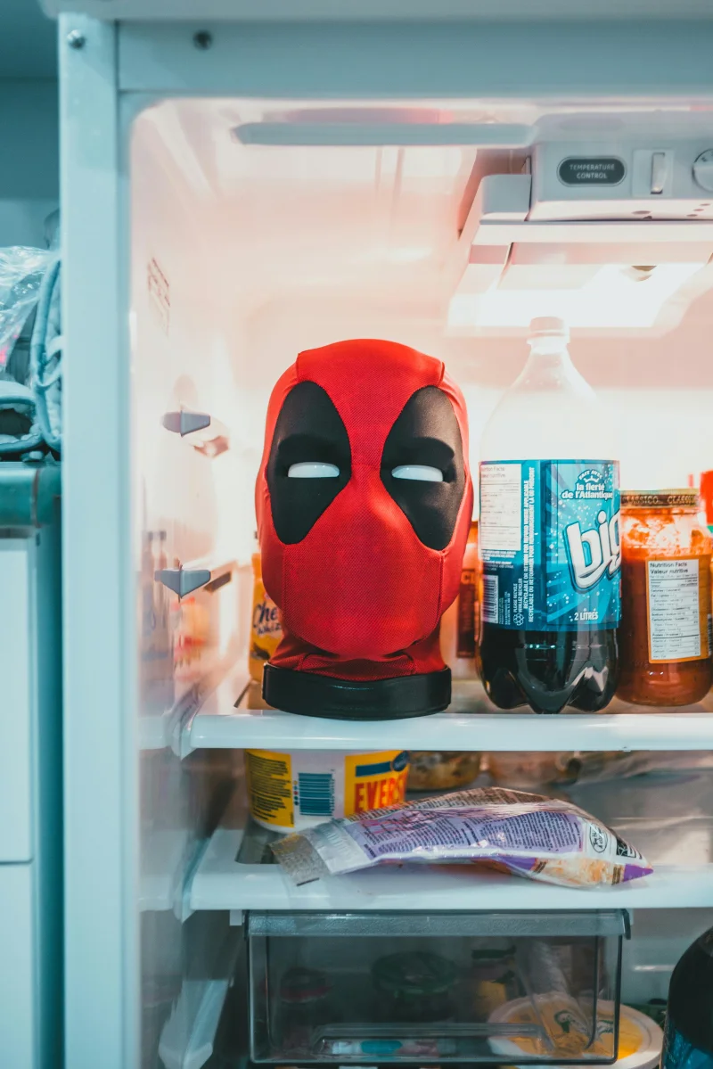 A red superhero-style mask inside a refrigerator alongside soda bottles and condiments.