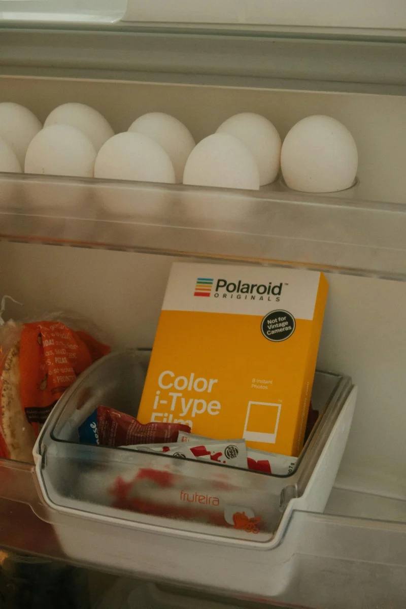 Interior view of a fridge showing a Polaroid film pack and eggs on the shelf.