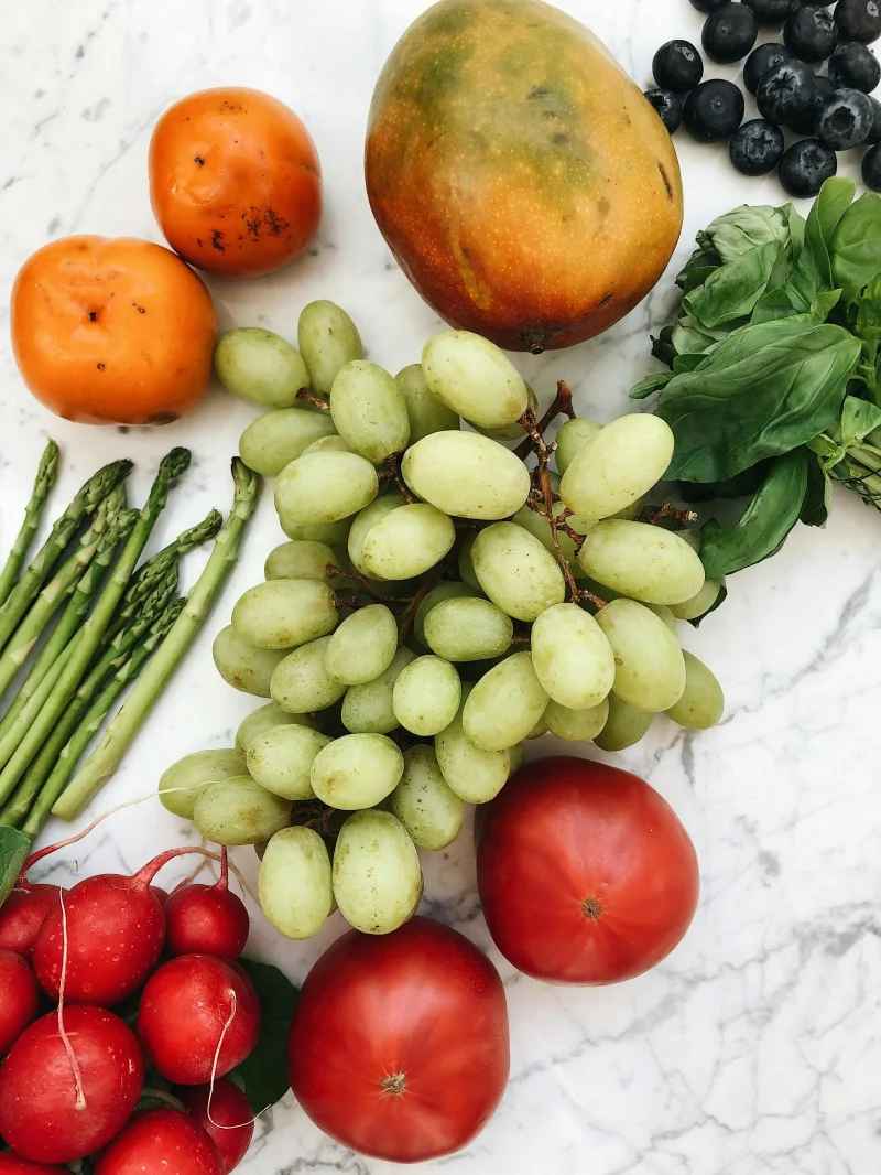 A vibrant mix of fresh fruits and vegetables including grapes, mango, and tomatoes on a marble surface.
