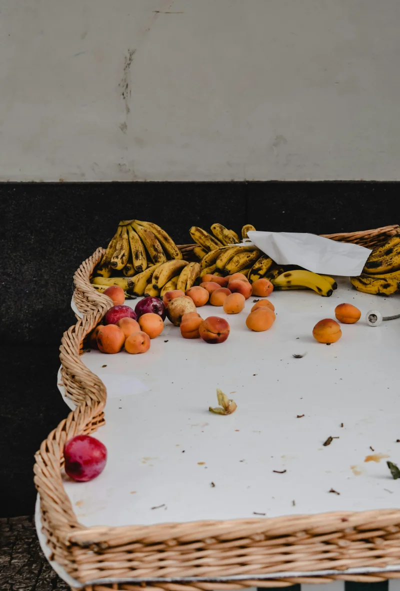 A display of fresh bananas and apricots in a woven basket on a street market table.