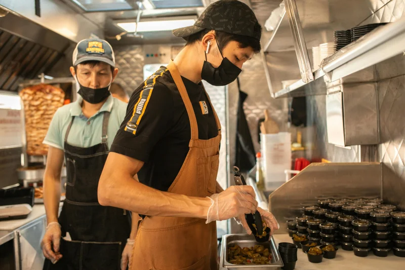 Two chefs prepare food in a food truck, highlighting teamwork and culinary skills.