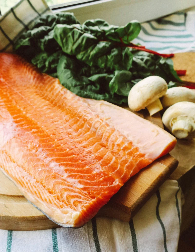 A fresh raw salmon fillet on a cutting board with spinach and mushrooms, ideal for healthy cooking.