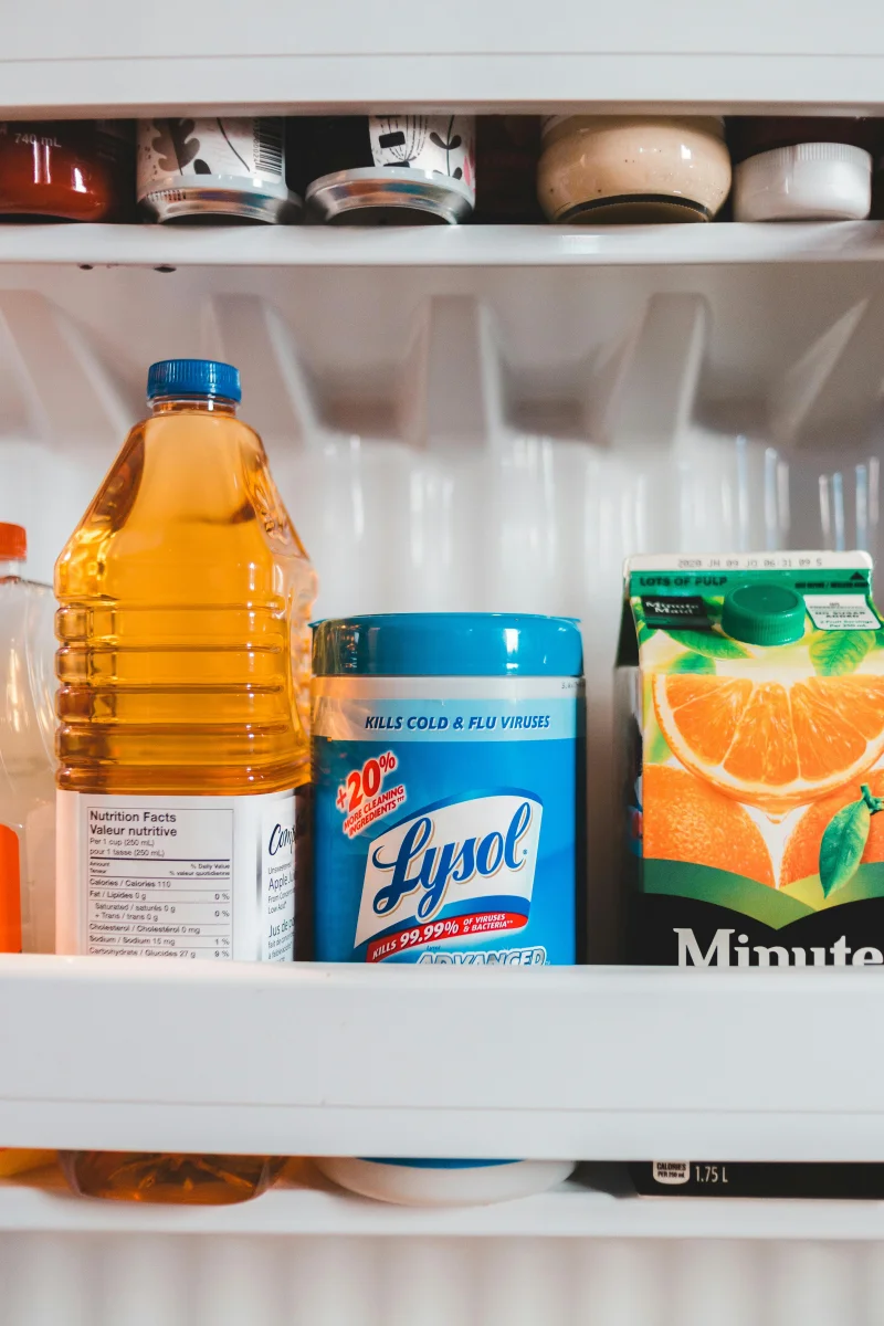 Close-up of fridge shelf with cleaning products and beverages for home organization and hygiene.