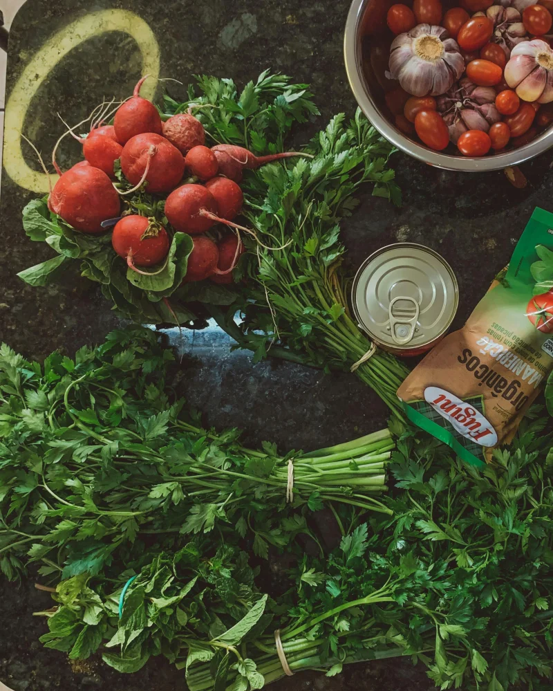 Fresh radishes, parsley, garlic, and tomatoes arranged on a kitchen counter for a rustic culinary setup.